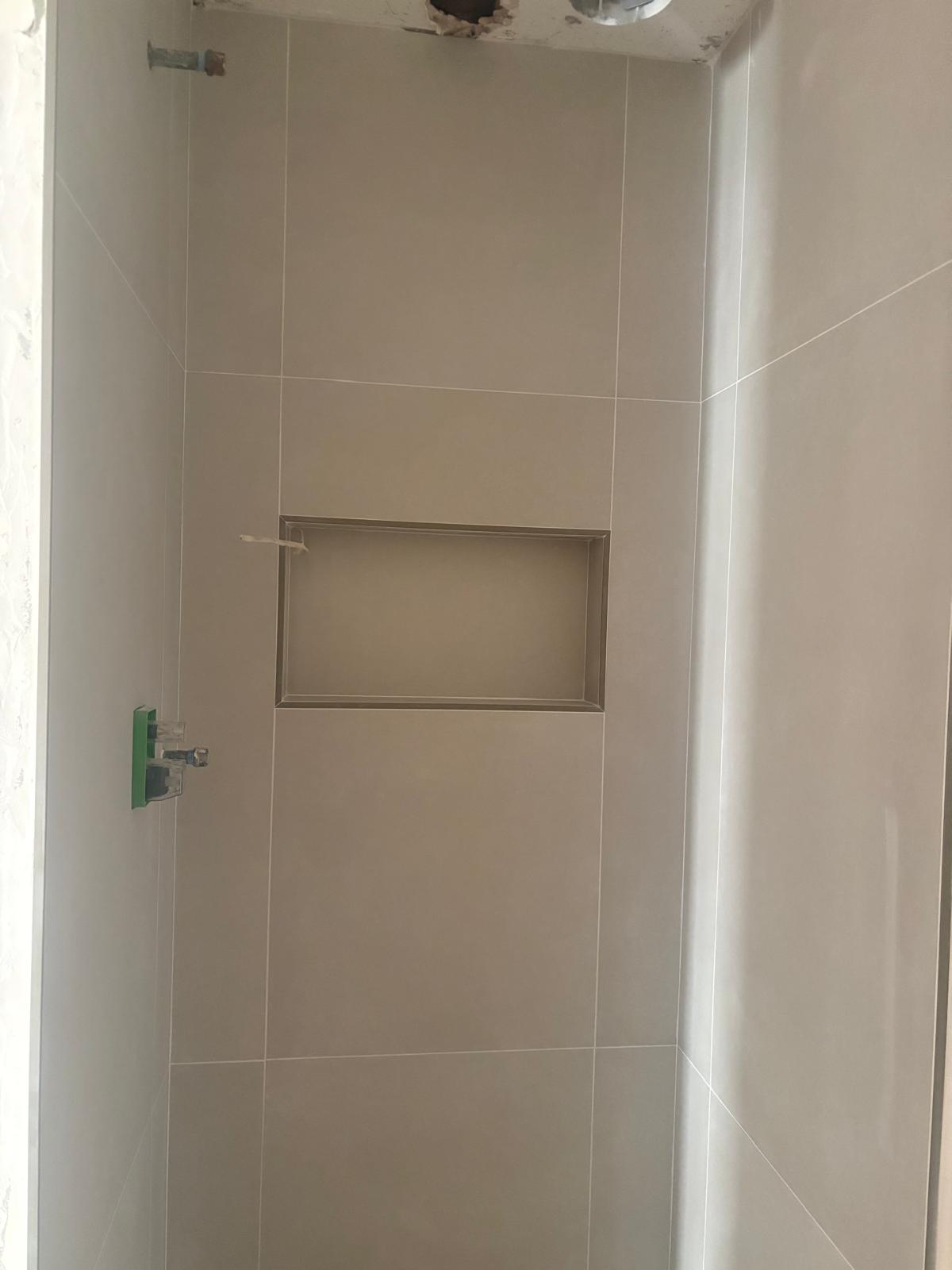 Shower in large beige porcelain tile with a rectangular recessed niche, mid-installation