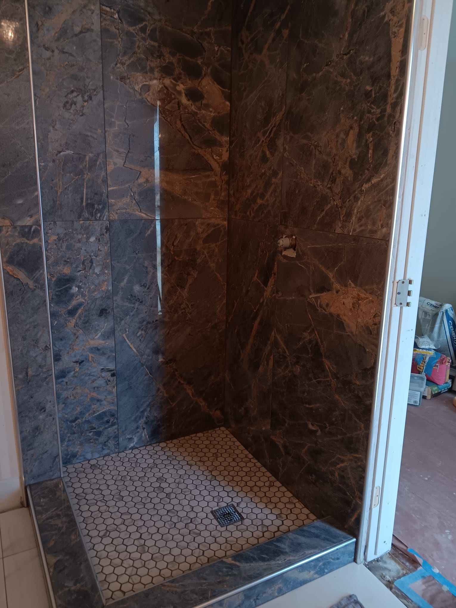 Shower in dark marble-look slabs with a white hexagon mosaic floor and matching curb