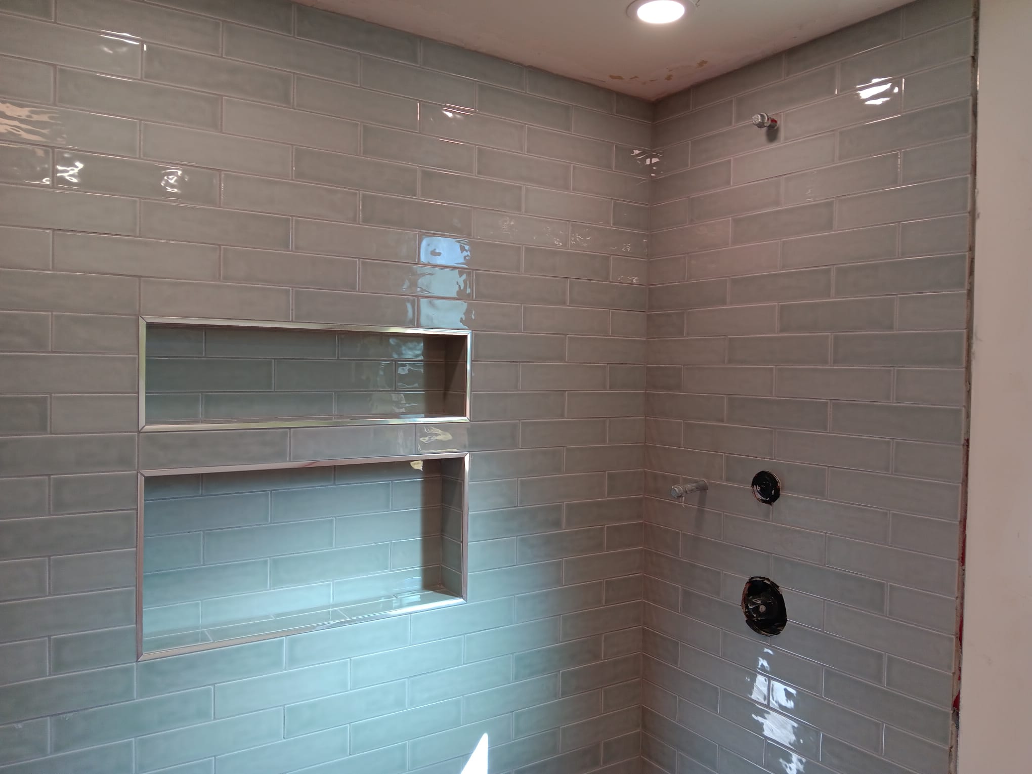 Shower wall in glossy grey-green subway tile with a long double recessed niche