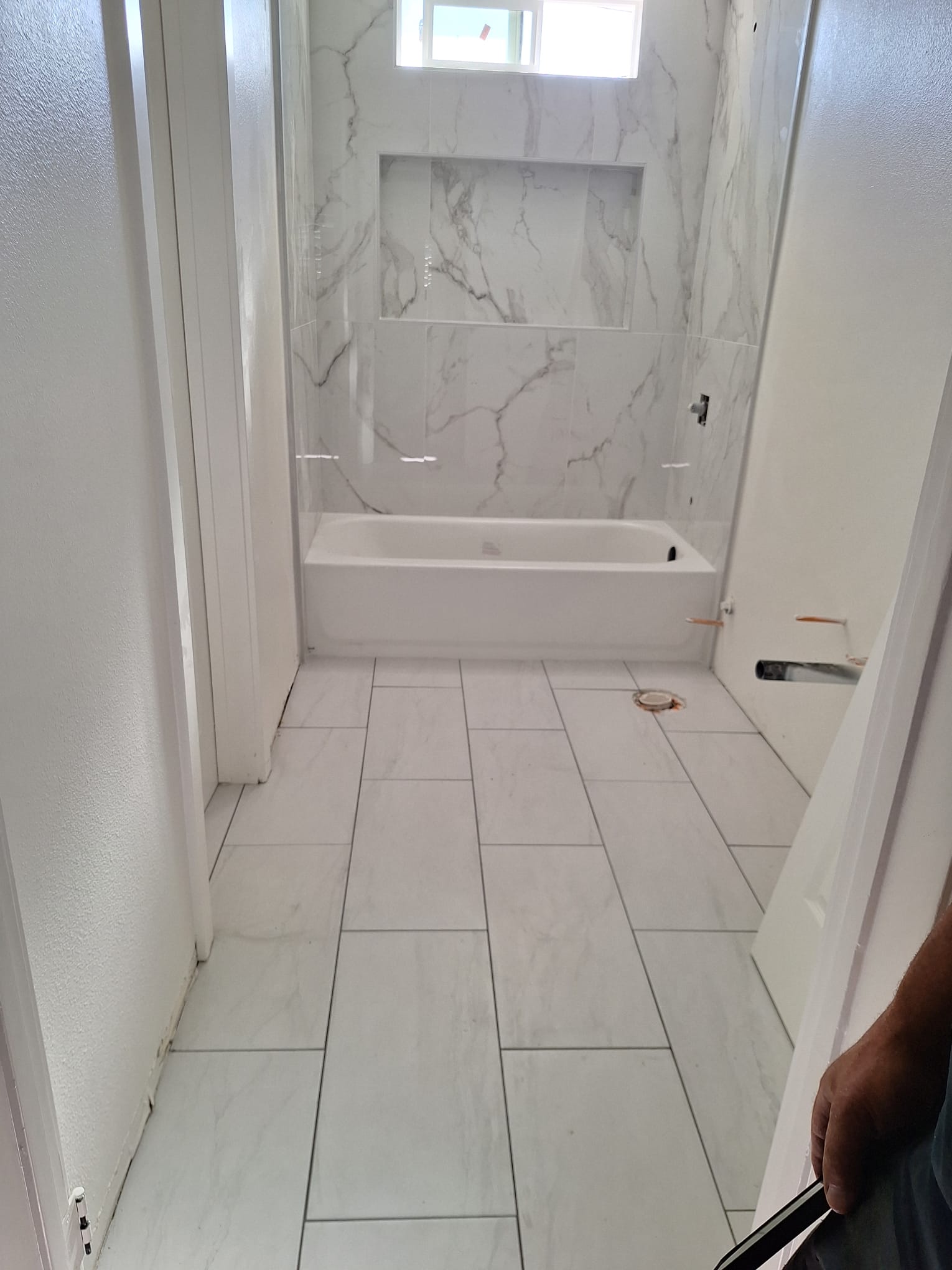 Bathroom floor in marble-look porcelain plank laid in a staggered pattern up to the tub