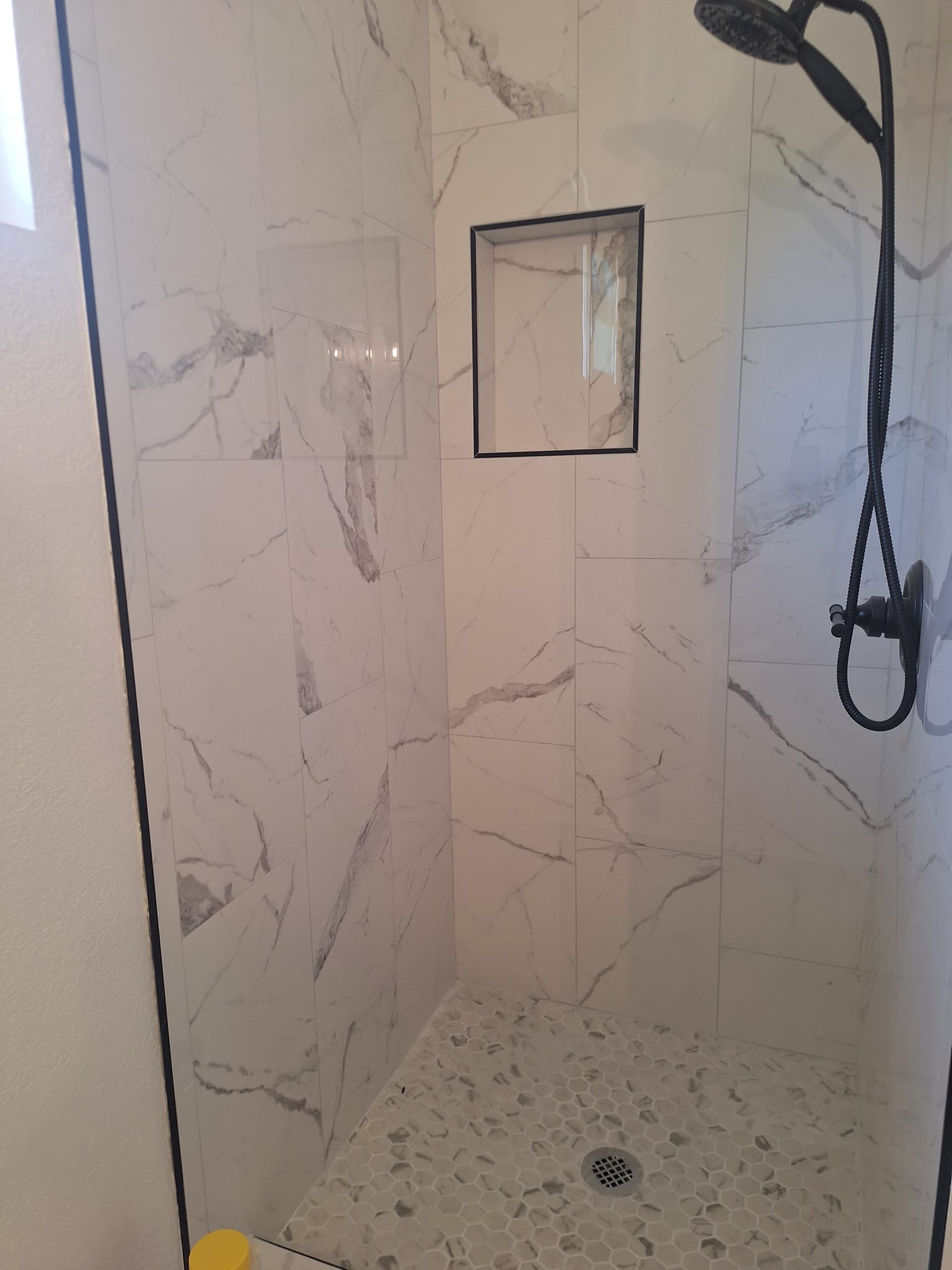 Shower in white marble-look porcelain with a black-trimmed niche and pebble floor