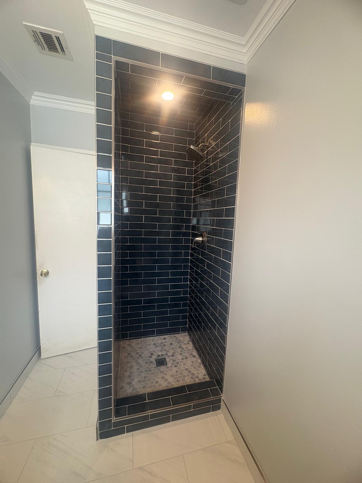 Walk-in shower in navy blue gloss subway tile with a grey hexagon mosaic floor