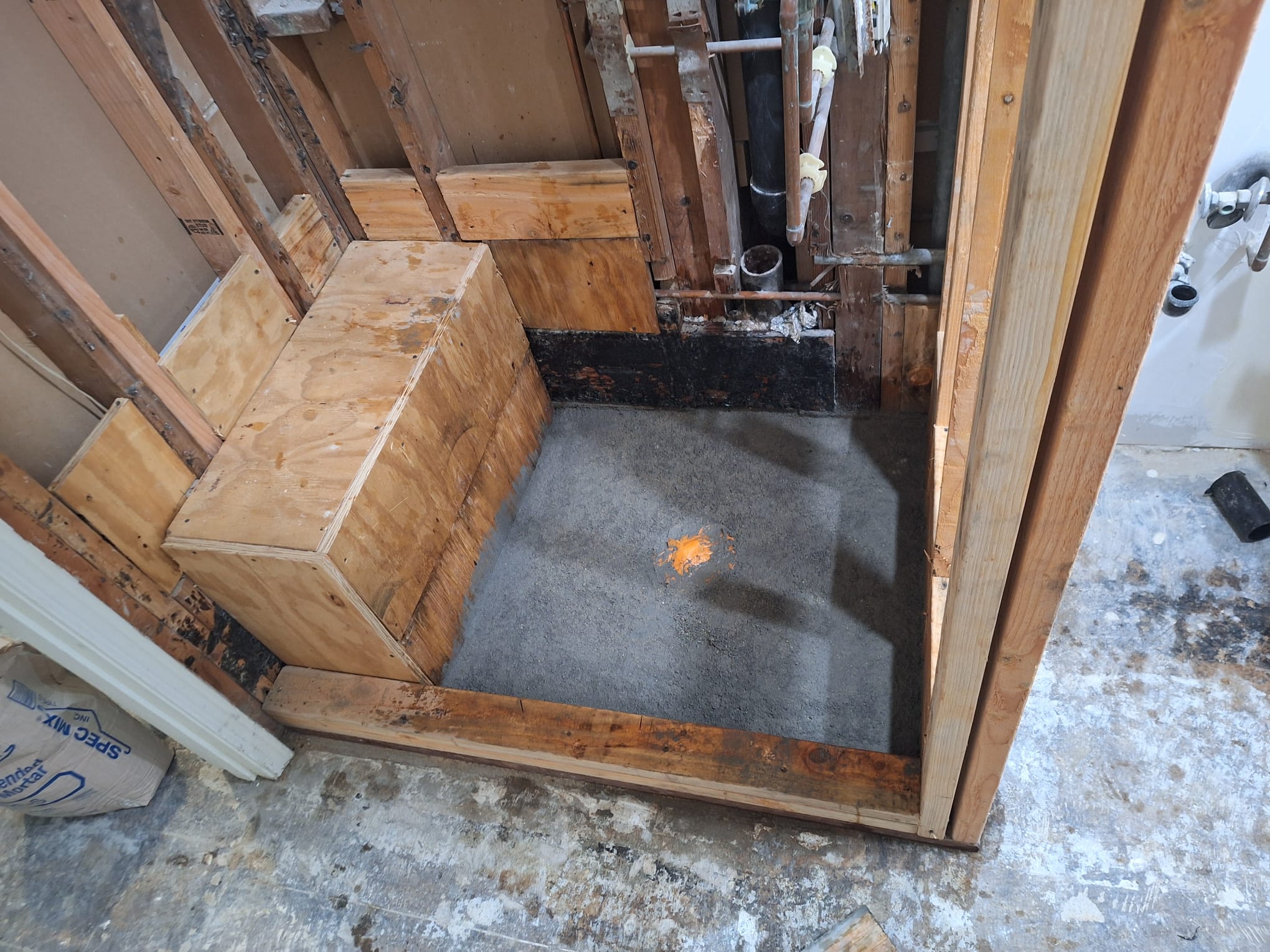 Shower opened down to the studs with a new plywood bench frame and a fresh mortar pan ready for waterproofing