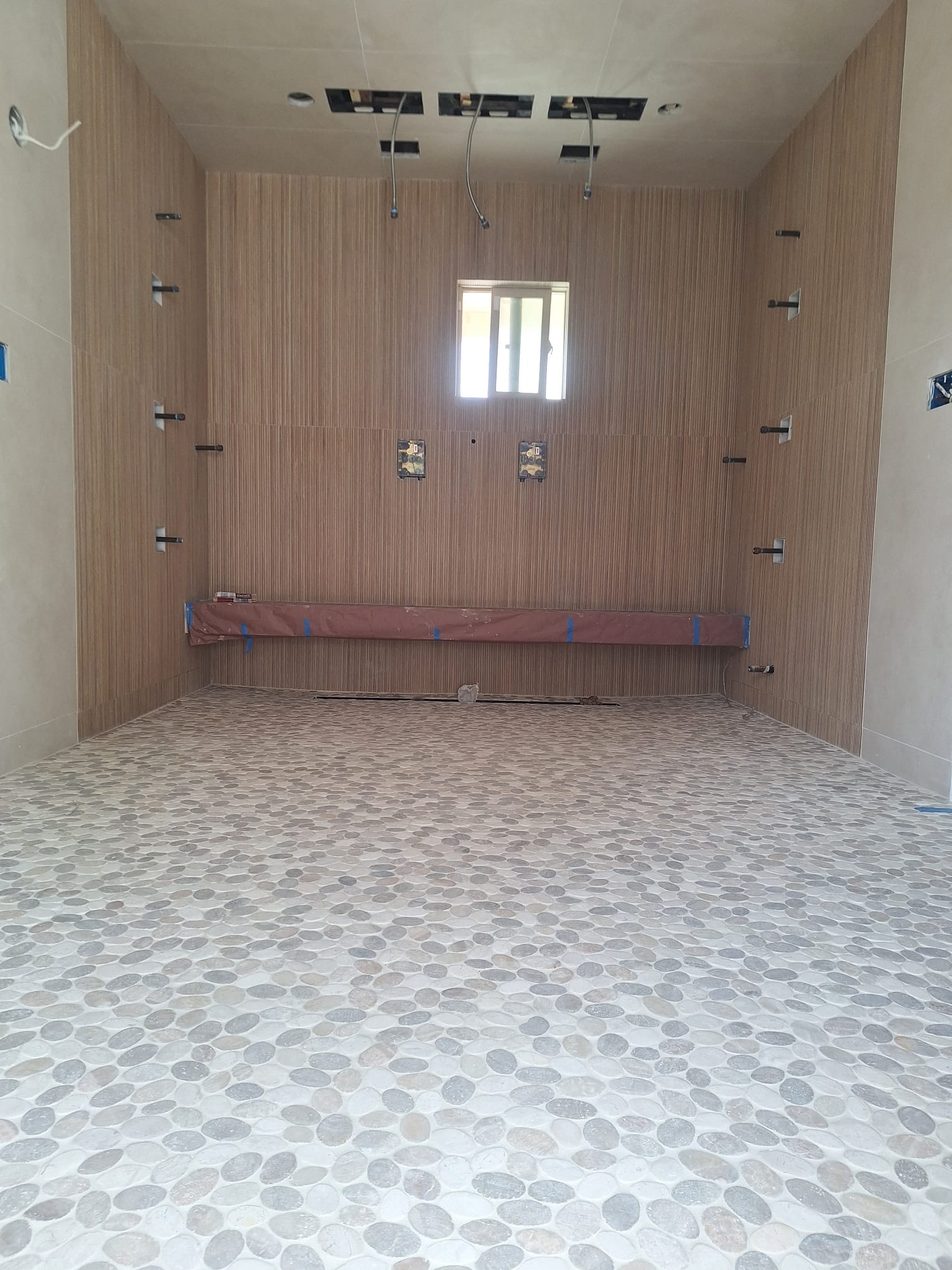 Large curbless wet room with river-pebble mosaic floor, linear drain, fluted wall tile and a built-in bench