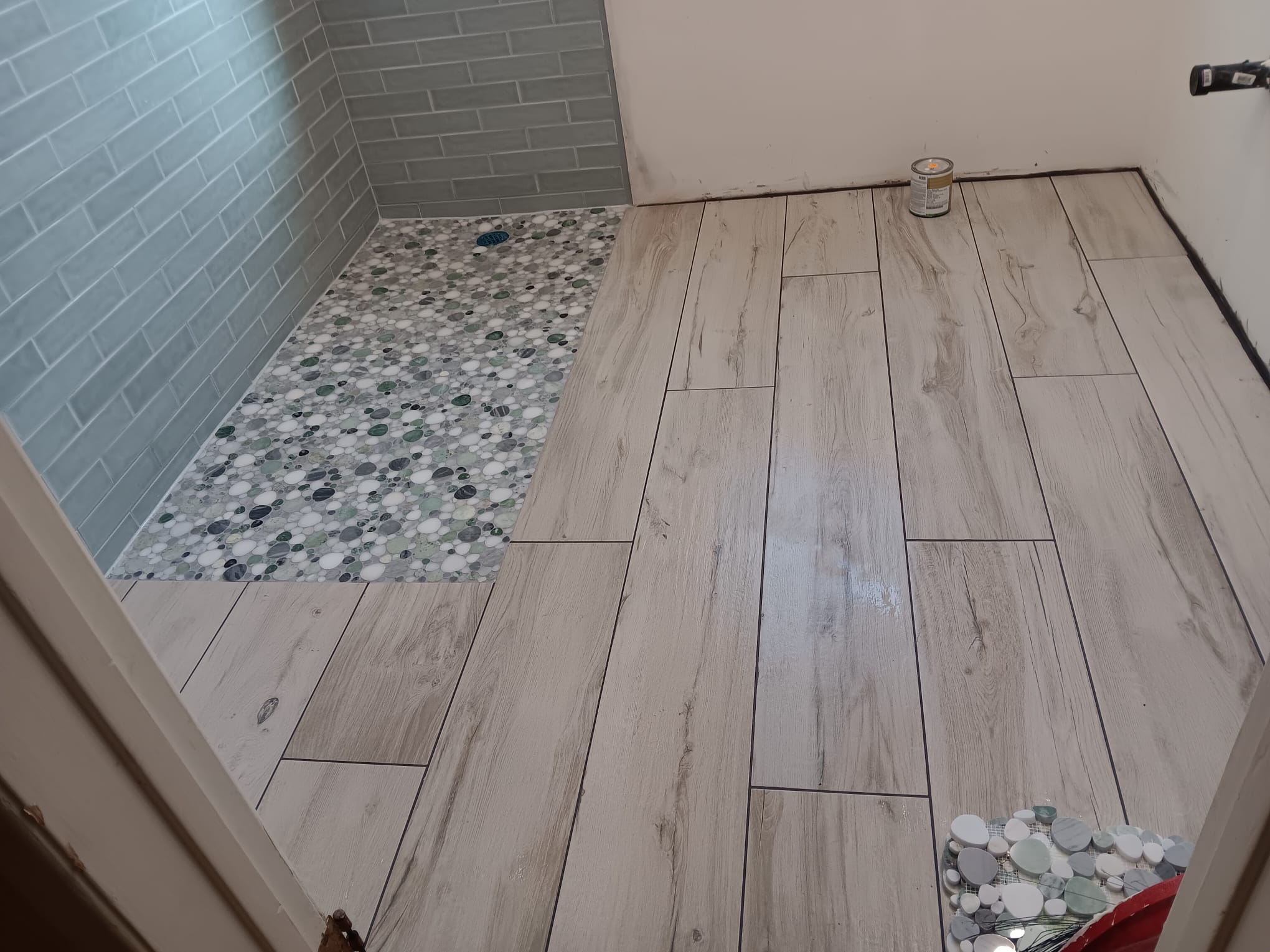 Bathroom floor in wood-look porcelain plank meeting a river-pebble shower floor